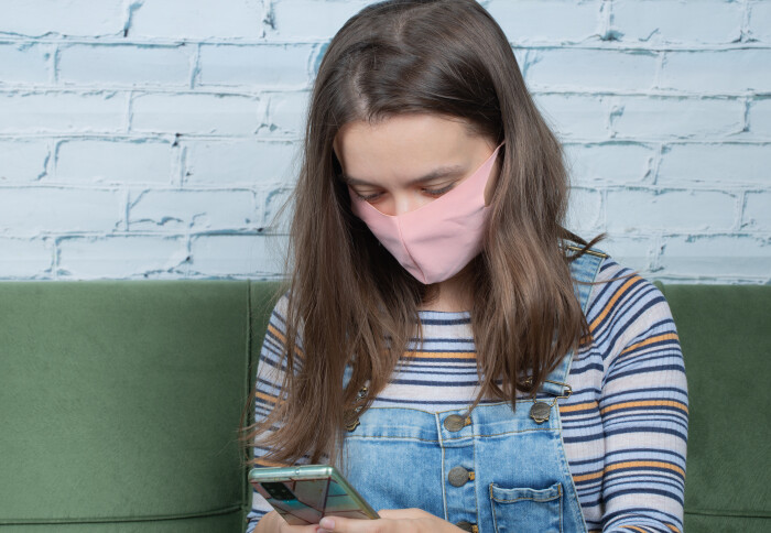 Teenage girl with face mask using mobile phone