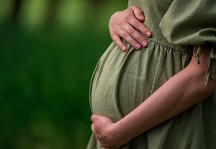 A woman in a green dress holding her pregnant belly