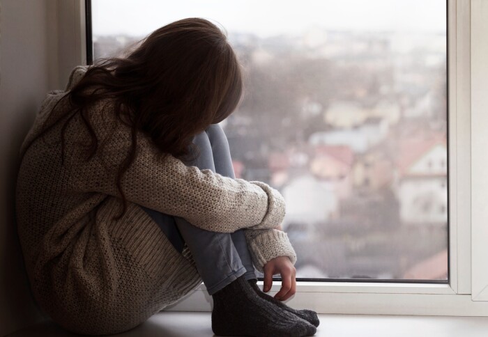 An unhappy young person sitting by a window.