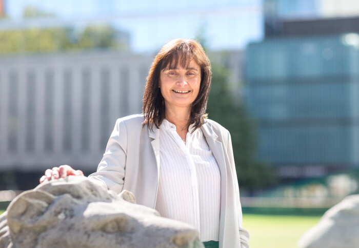 Michele Dougherty with her hand on a stone lion with buildings in the background