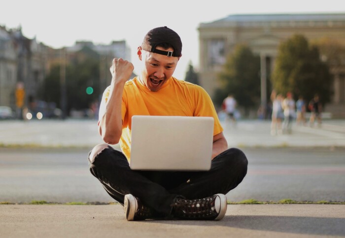 Happy student sitting cross-legged with laptop outdoors