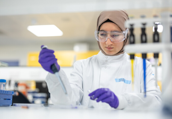 A student in a lab coat and goggles doing laboratory work.