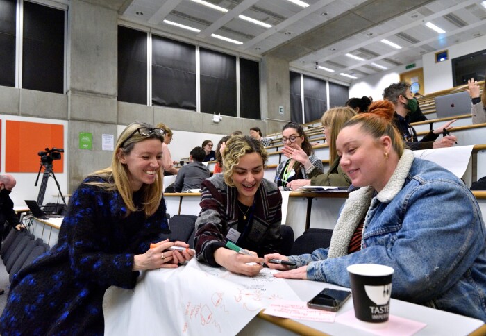 Three women sat in a lecture theatre at Imperial College smiling and talking