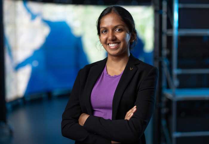 woman in business attire power posing with her arms crossed and smiling in front of a map of the world