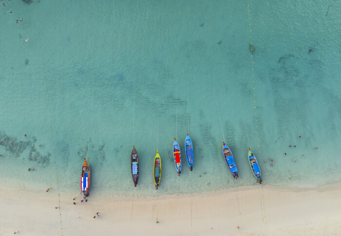 Drone view of tranquil beach with small boats in blue sea water.