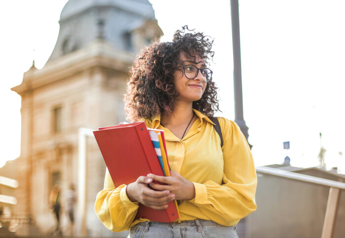 image of smiling student holding books and walking down an external staircase