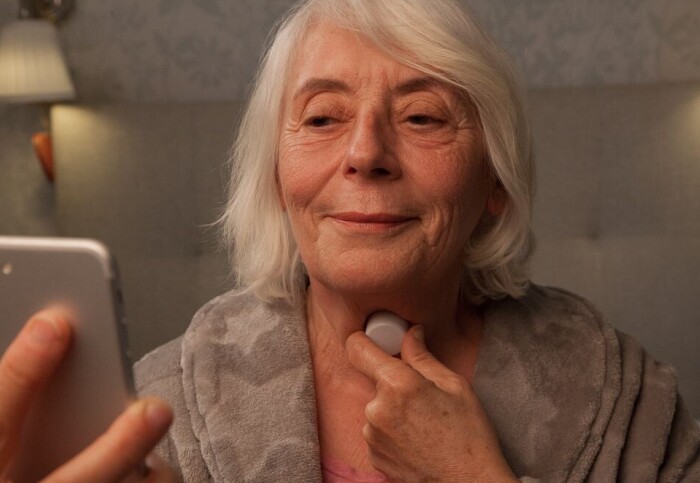 A woman holds a device to her neck while consulting a smartphone