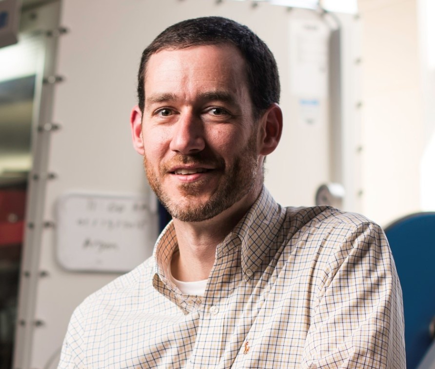 Portrait of Dr Doug Kelley. He is sat in a mechanical engineering laboratory. 