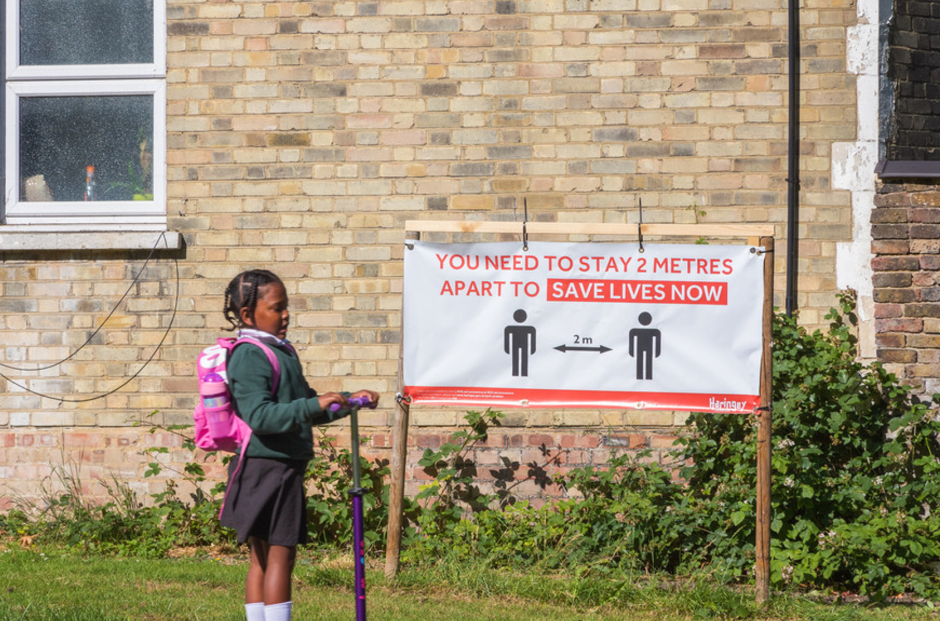 School girl riding a scooter past a COVID-19 sign