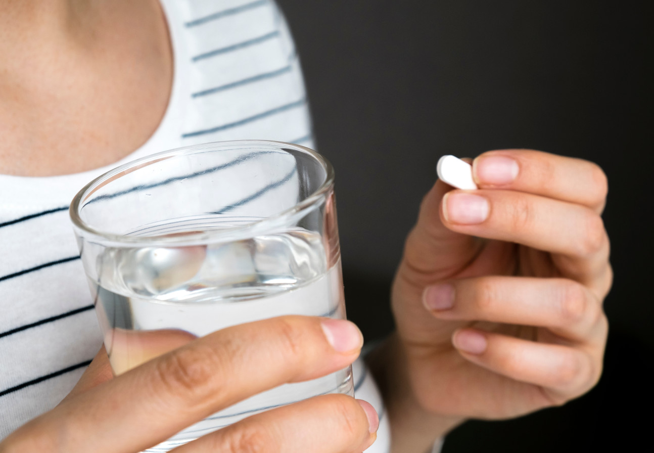 A woman holding a pill and a glass of water