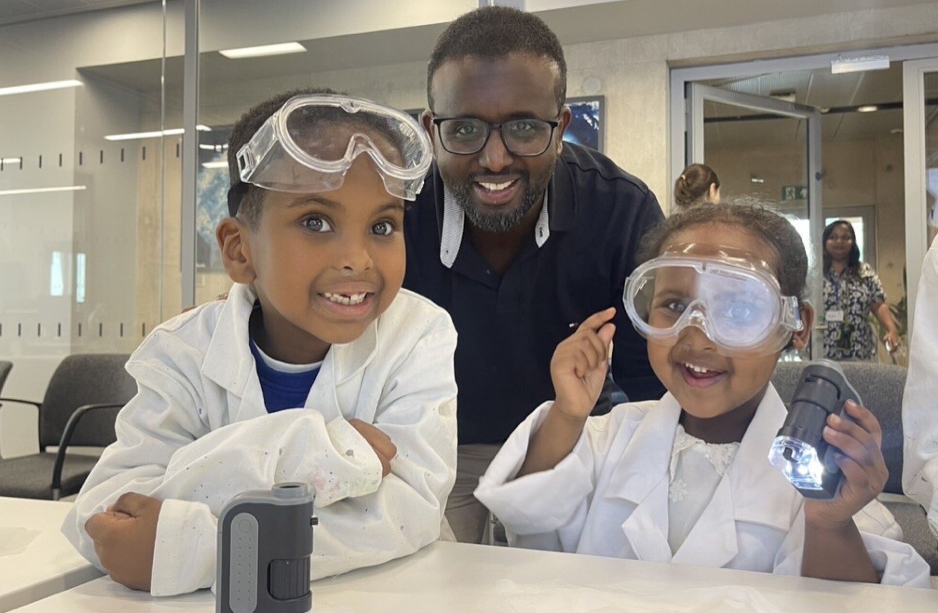 Father and two children wearing lab coats and safety goggles