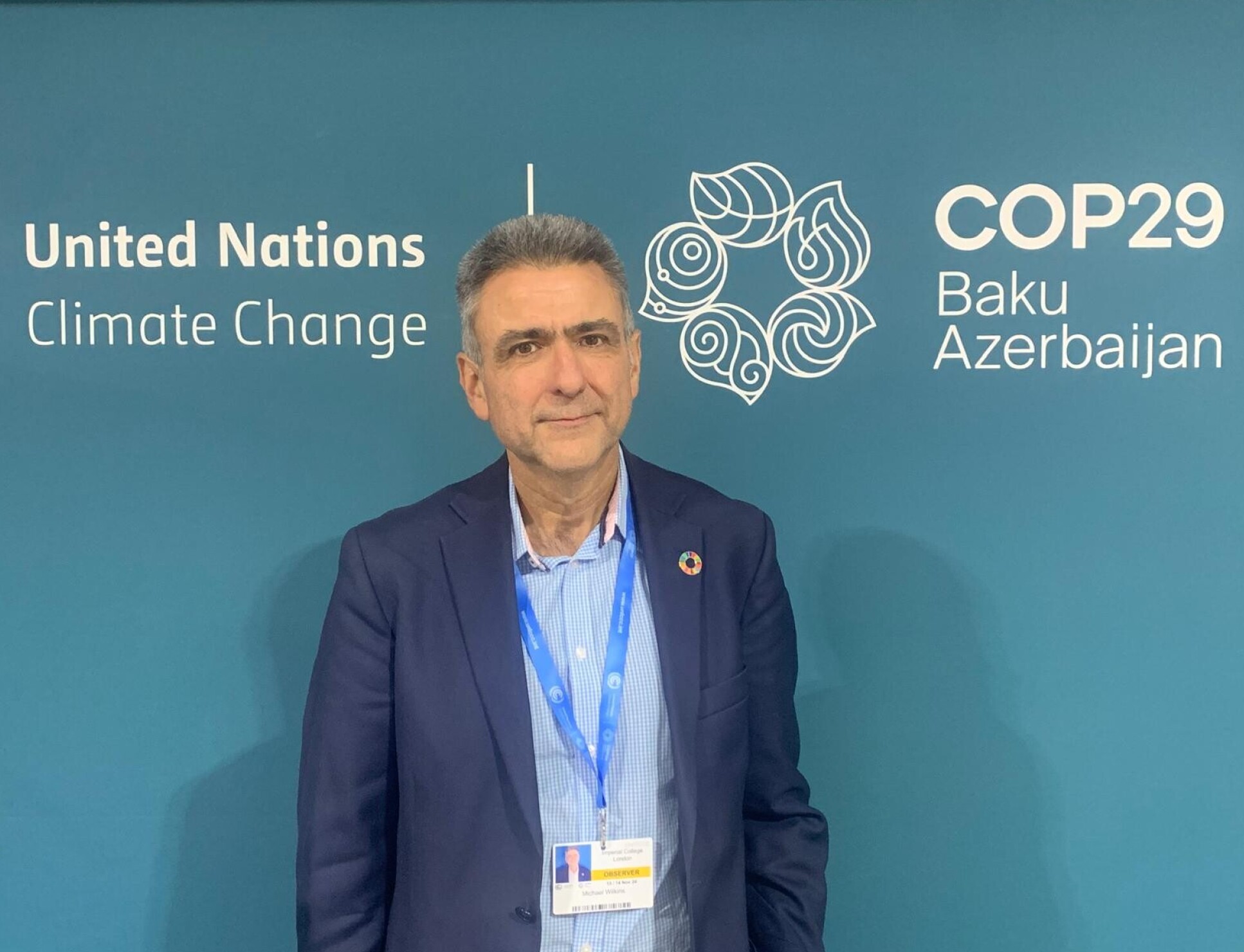 A photo of Mike Wilkins infront of signage at COP29