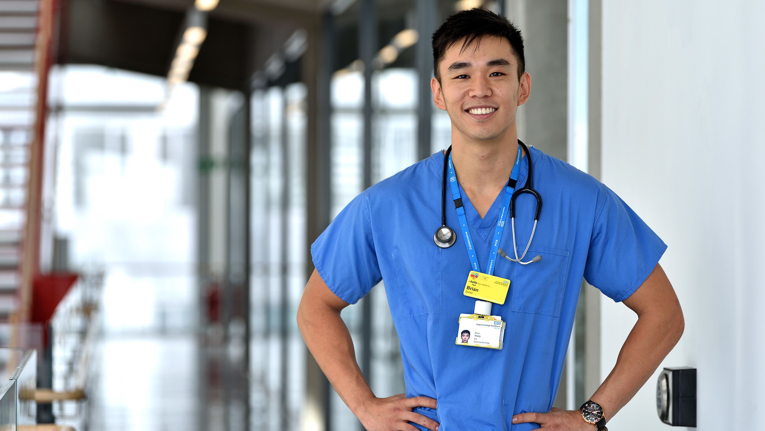 Dr Brian Wang, dressed in scrubs with a stethascope around his neck, smiles towards the camera