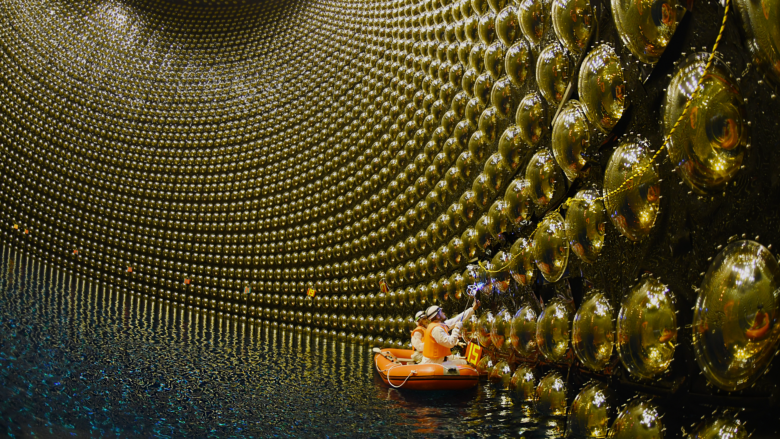 Two scientists work on the reactor from a boat in the water, a huge concave shape with what looks like giant silver balls on the walls