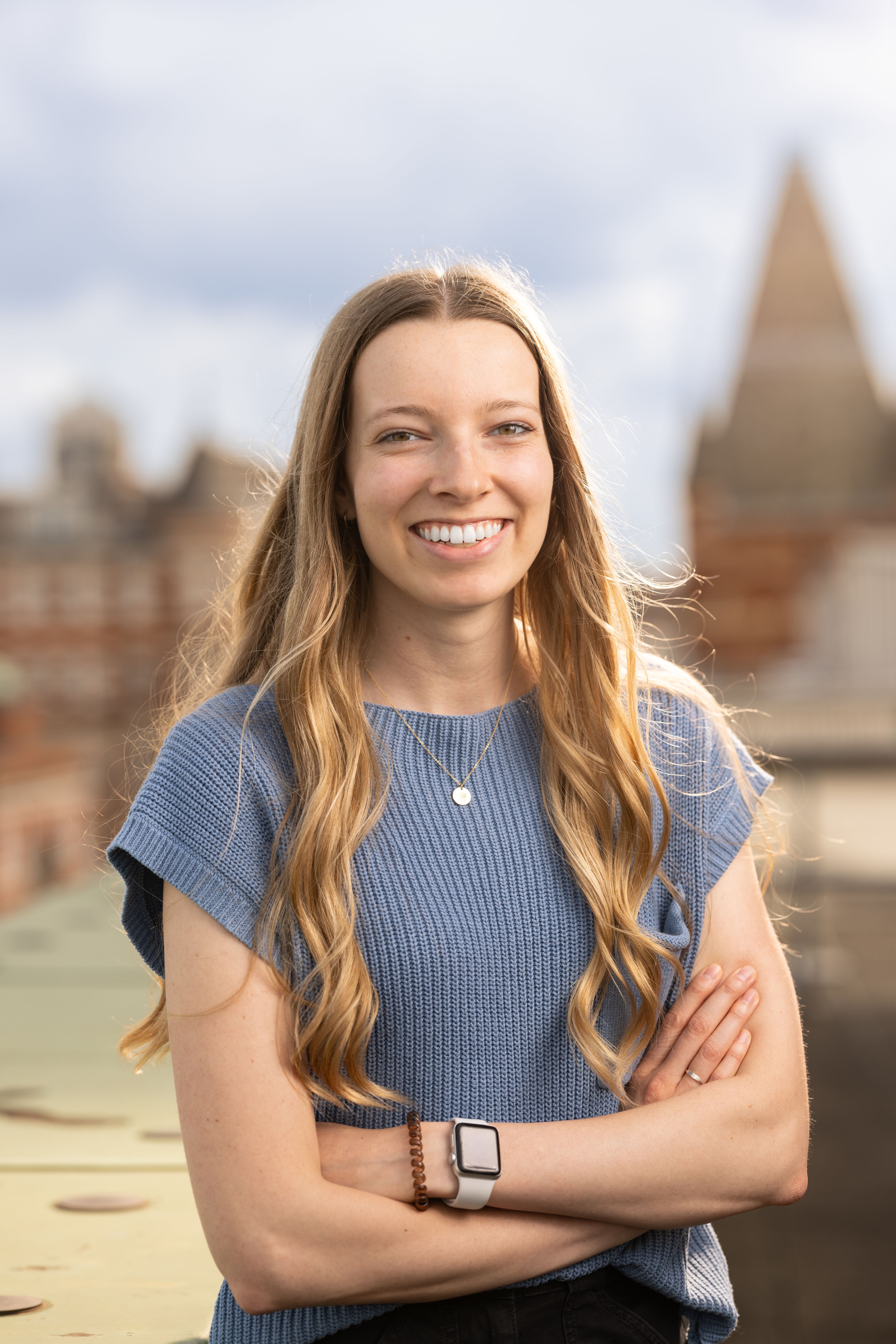 McKenna standing on a rooftop terrace in front of buildings around South Kensington campus, wearing a grey knit short-sleeved top and a silver necklace