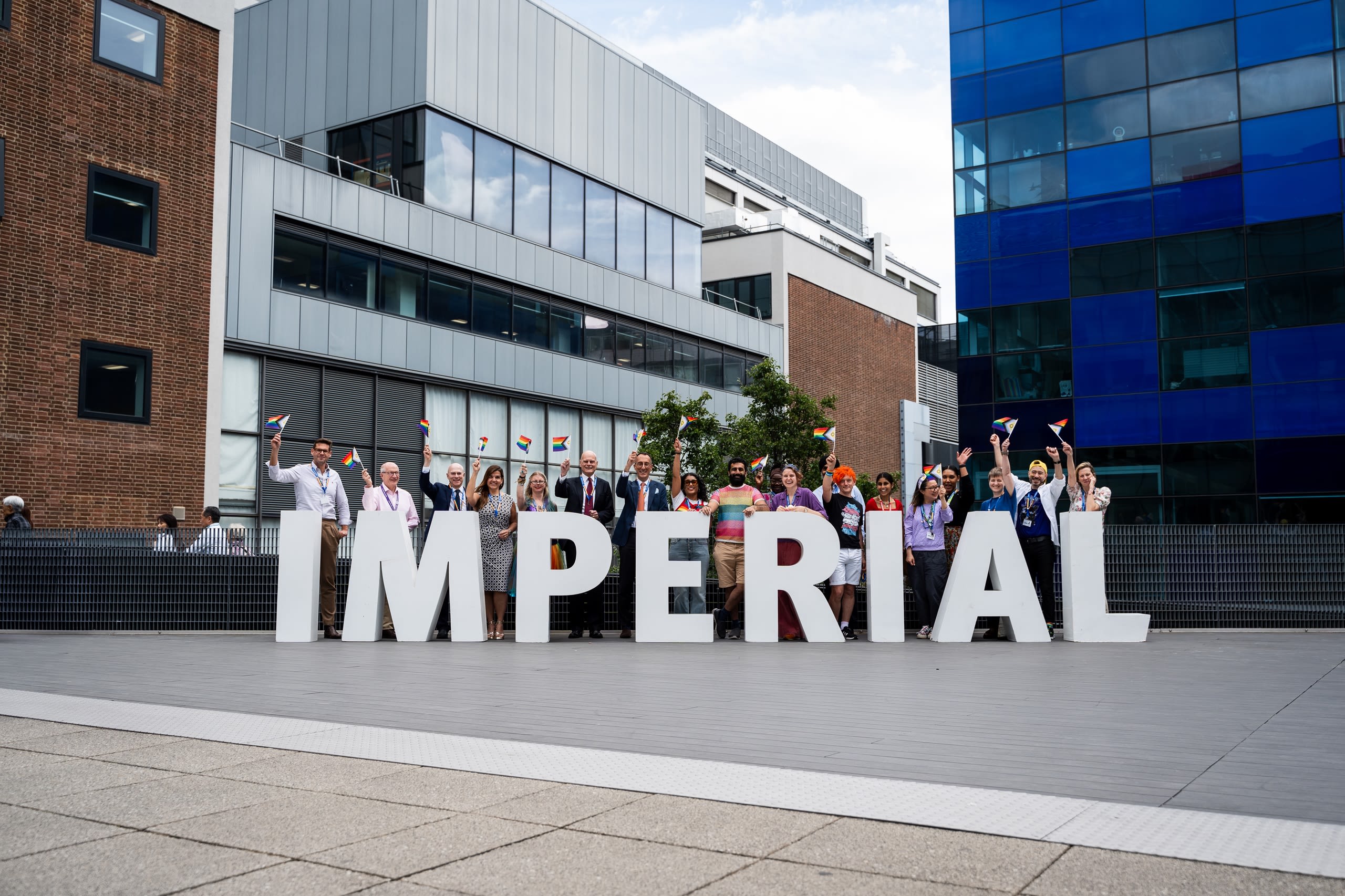People waving pride progress flags behind giant letters spelling out Imperial