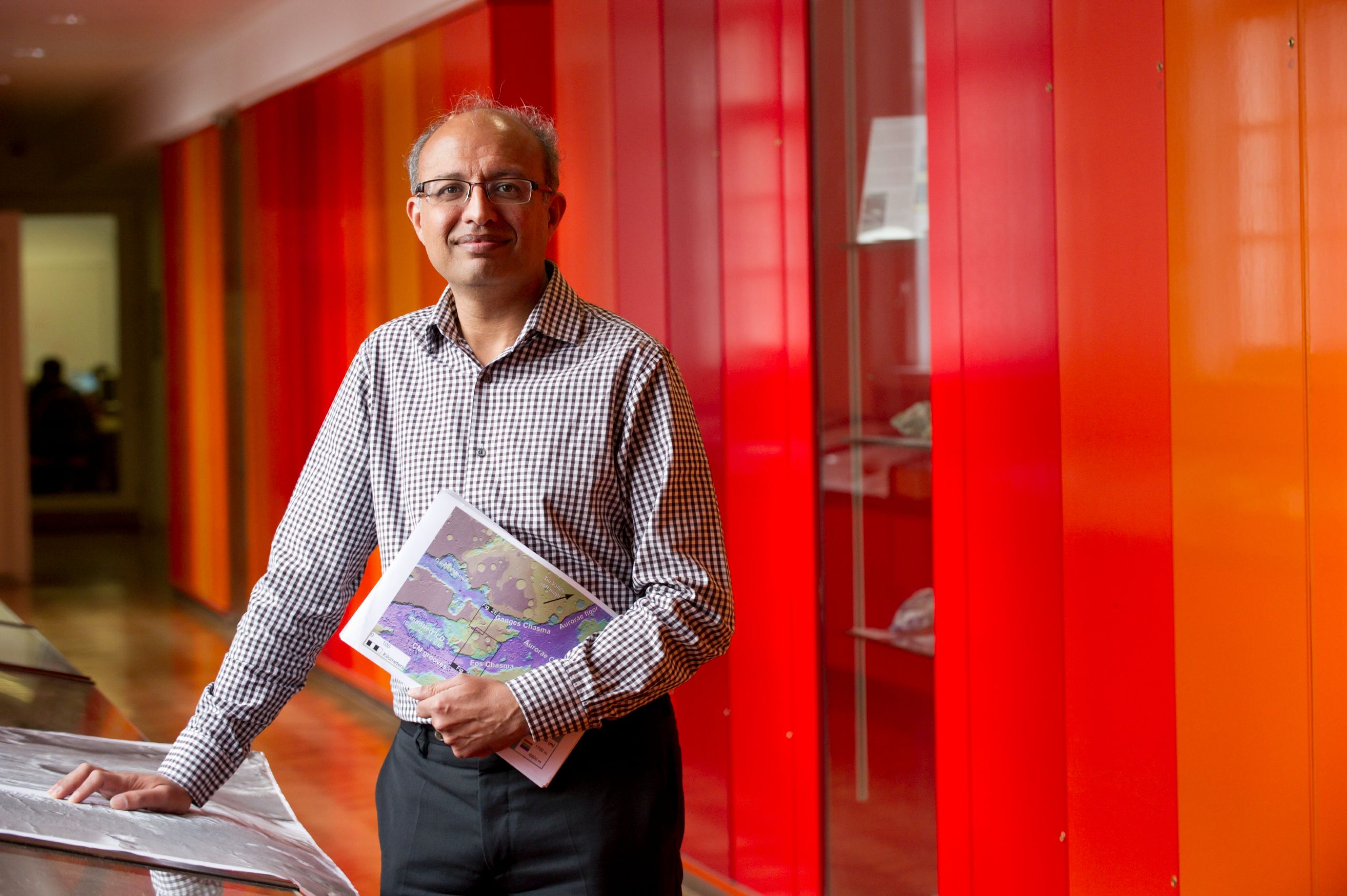 Professor Sanjeev Gupta stands in the Faculty of Engineering against dark red panelling