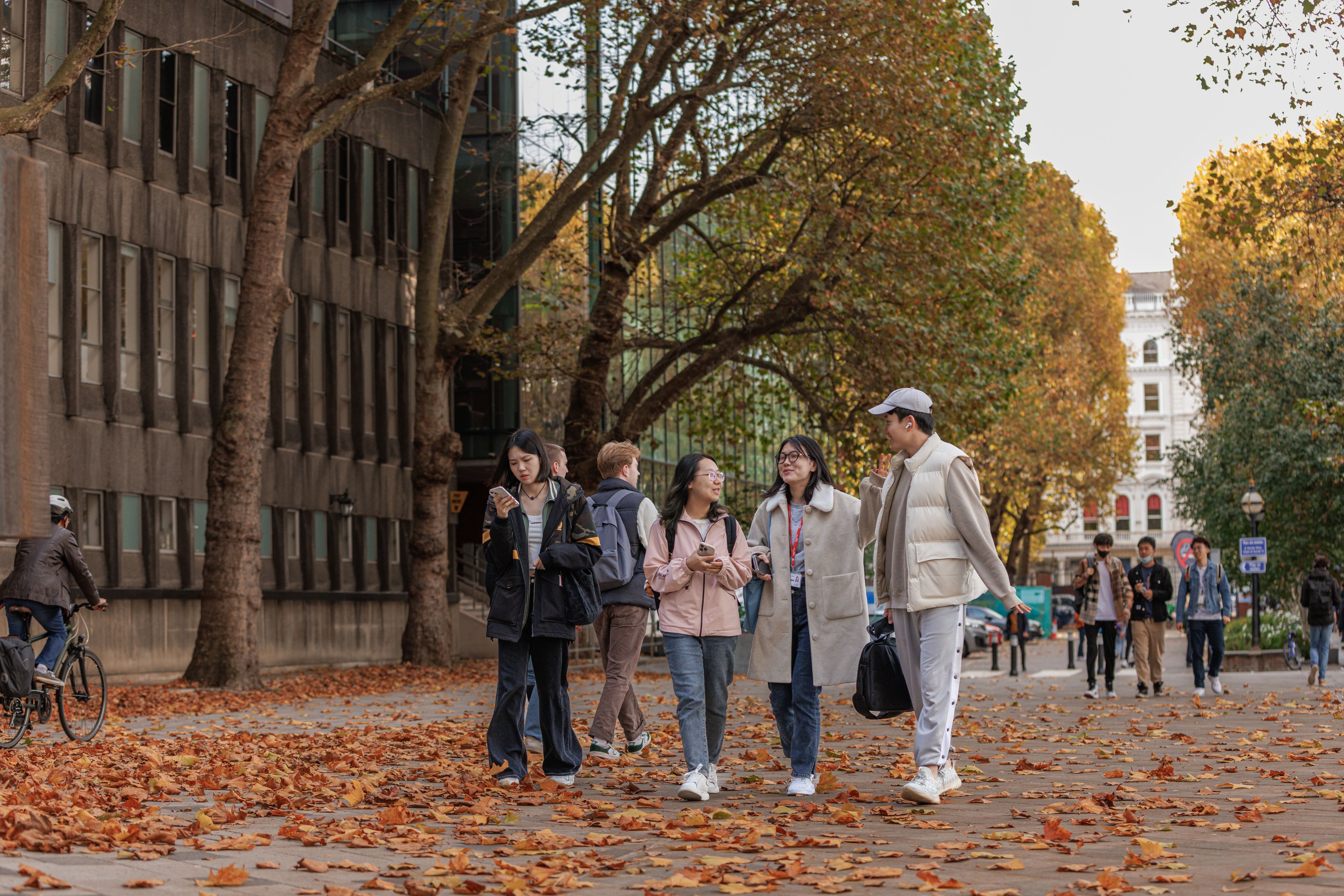 A group of students walk across an autumnal Dangoor Plaza. Leaves are littering the ground.