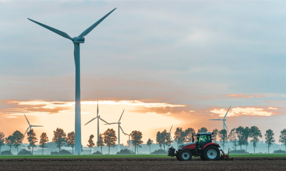 A windfarm behind a tractor ploughing a field
