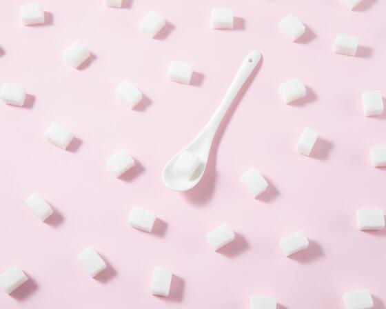 White sugar cubes and a teaspoon on pastel pink background