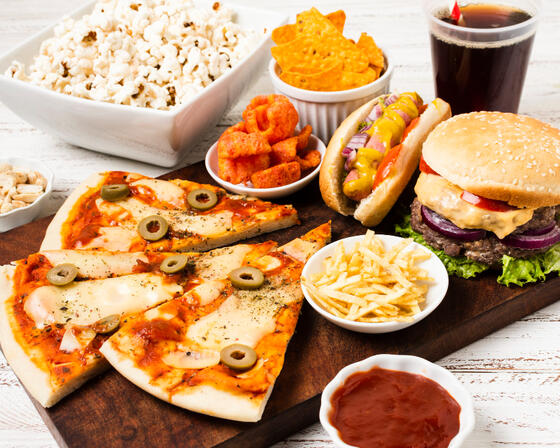 A photo of a selection of fast foods, including slices of pizza, French fries, burgers, crisps and fizzy drink