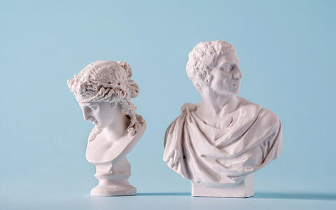 Two white Roman or Grecian antique style busts of young people over a blue background