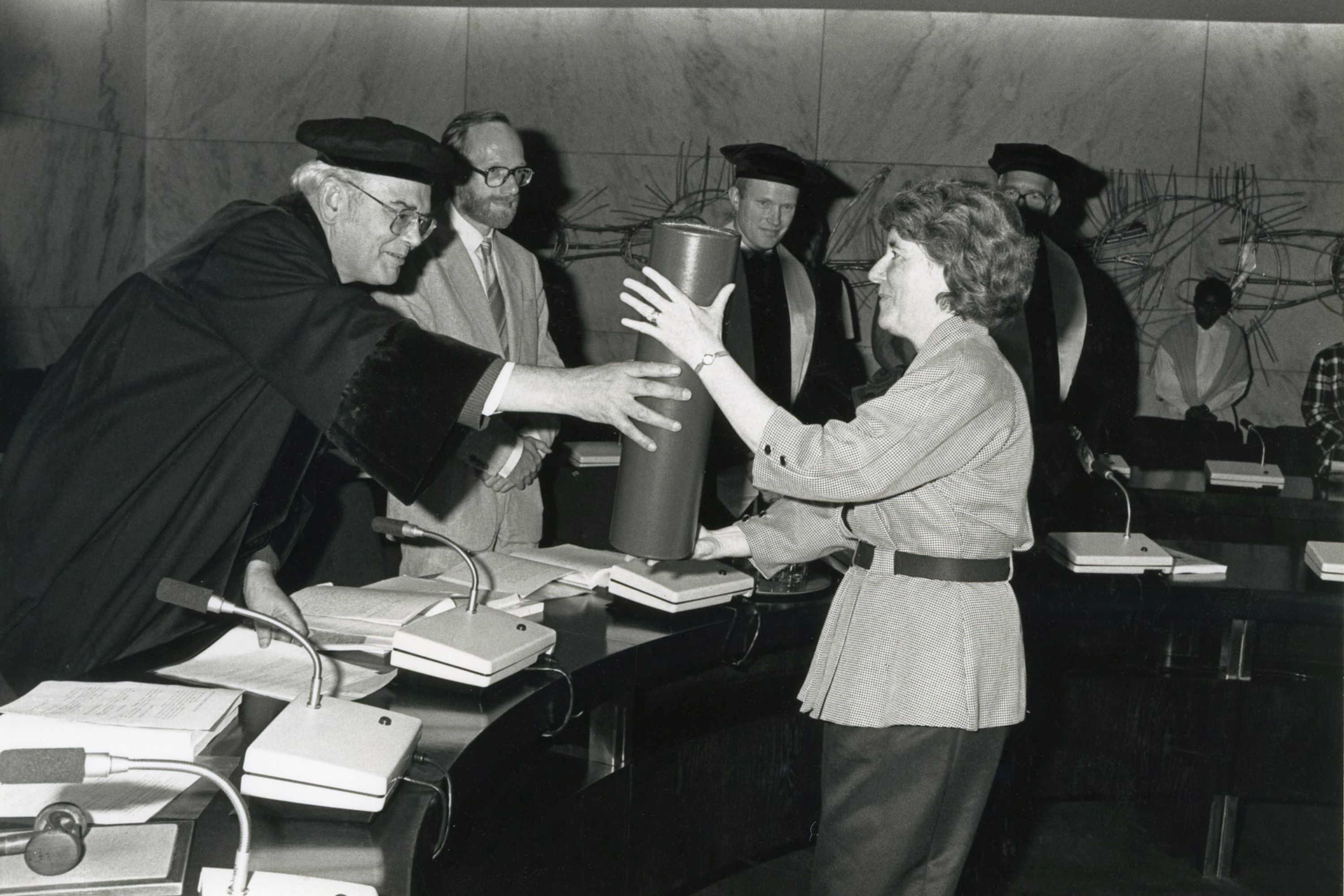 Black and white photo of Professor Frize exchanging a large cylindrical item with an academic wearing a gown