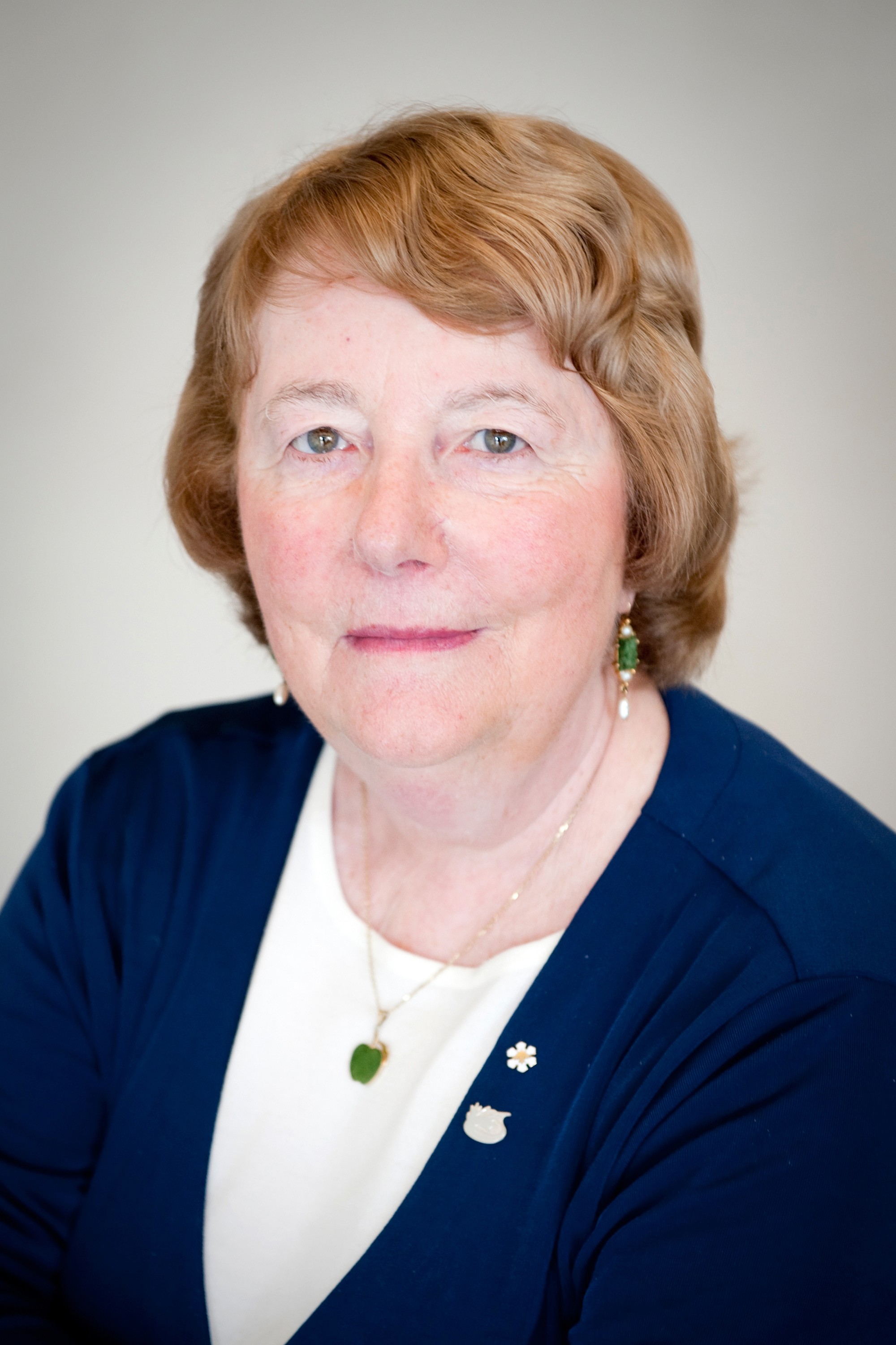 Headshot of Professor Monique Frize against a beige background. She is wearing a navy cardigan and a necklace with a pendant.