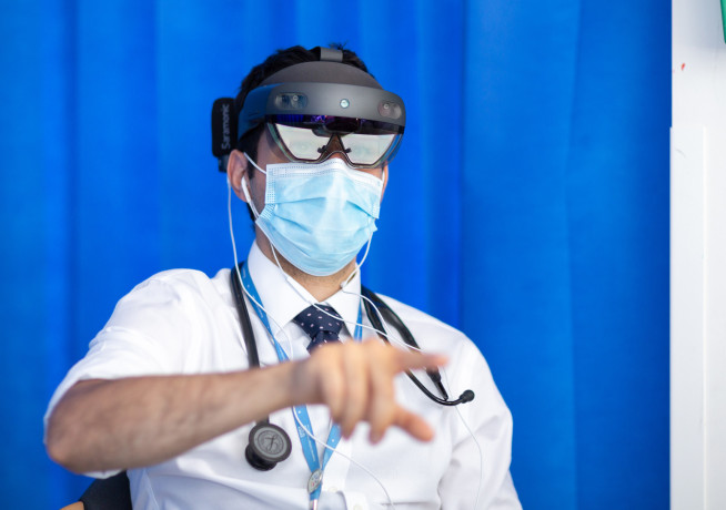 A doctor wearning a HoloLens VR device and headphones during a virtual ward round 
