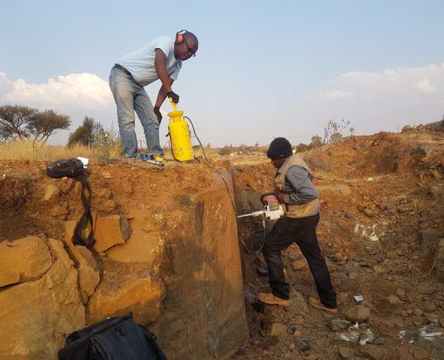 Two people drill into a rock with a small handheld drill in Botswana in the sunshine
