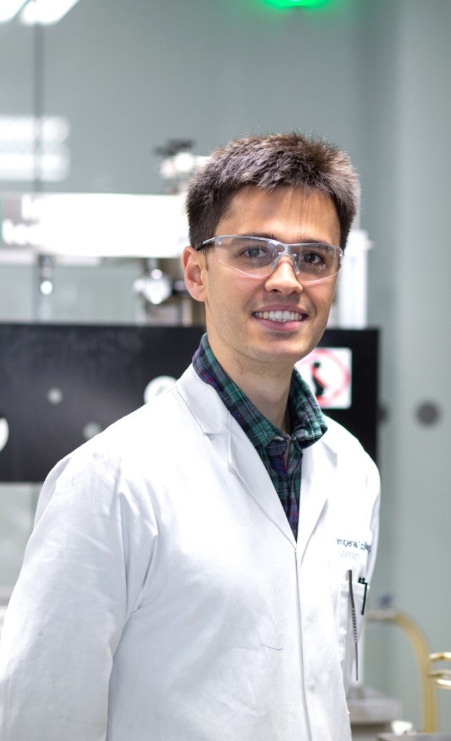 Student in a lab coat and goggles smiles at the camera