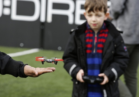Kid holding a remote control while a small drone flies off a man's hand in the foreground