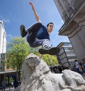 A parkour athlete leaps over the stone lion on Imperial's lawn