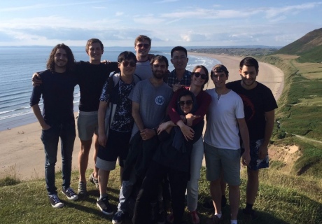 PE-CDT Cohort 8 students in group in front of sandy beach, with blue sky, Swansea