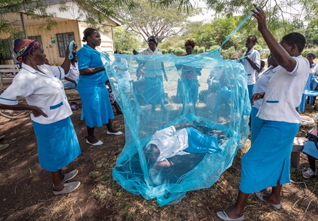 Aid workers explain how to use malaria nets to villagers