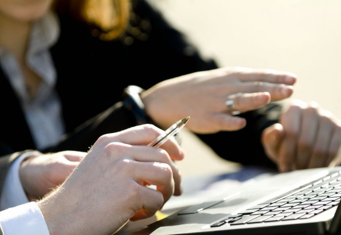 Two pairs of hands, one holding a pen, the other hovering over a keyboard