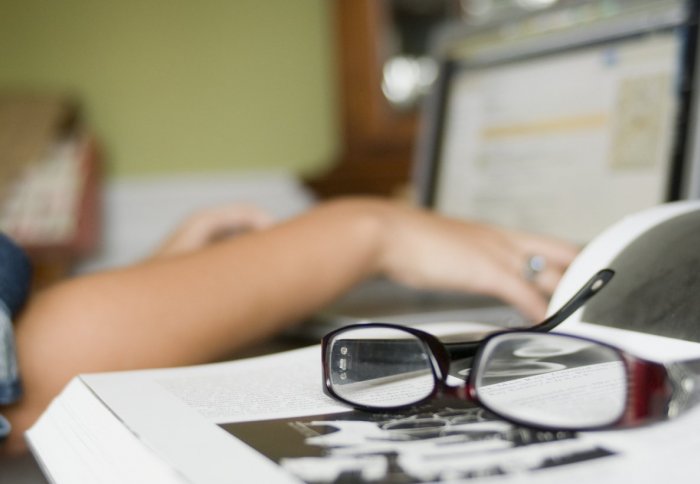 Pair of hands hovering over a laptop, with a medical book and glasses in the foreground