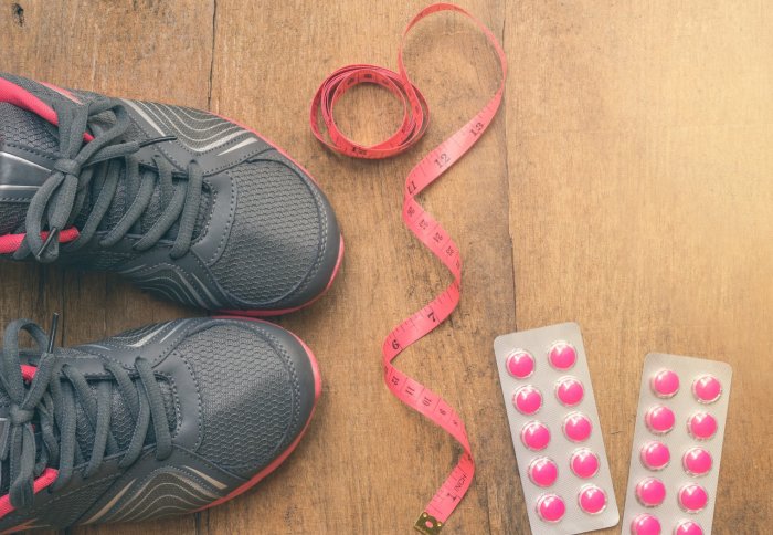 Running shoes, a tape measure, and some pills laid out on a wooden floor.
