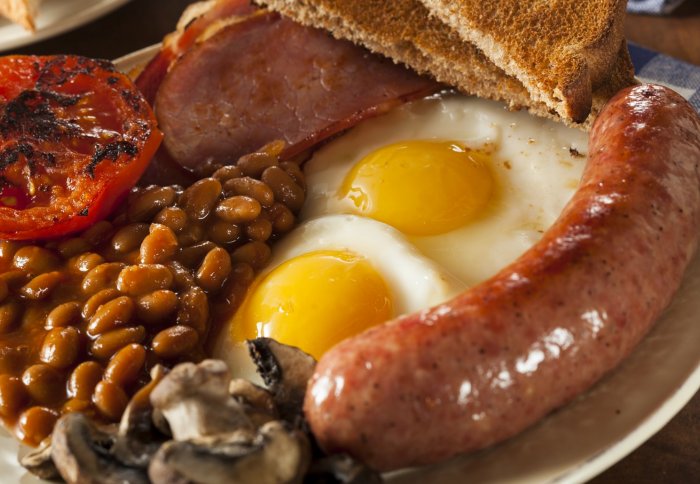 A greasy fried breakfast, consisting of two eggs, a sausage, beans, mushrooms, tomato and toast
