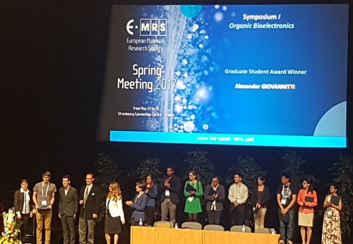 Prize winners on conference stage, with screen showing Alex Giovannitti's prize