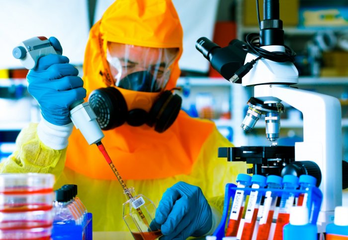 Scientist in yellow hazmat suit working with pipettes in a laboratory.