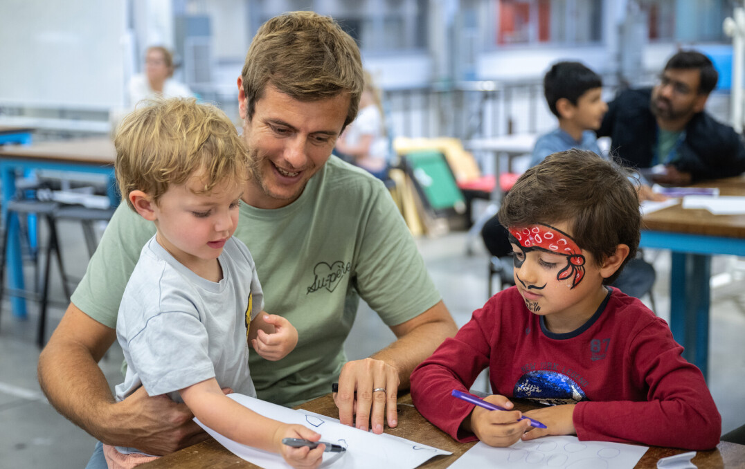 A parent/carer helping two children with a drawing activity