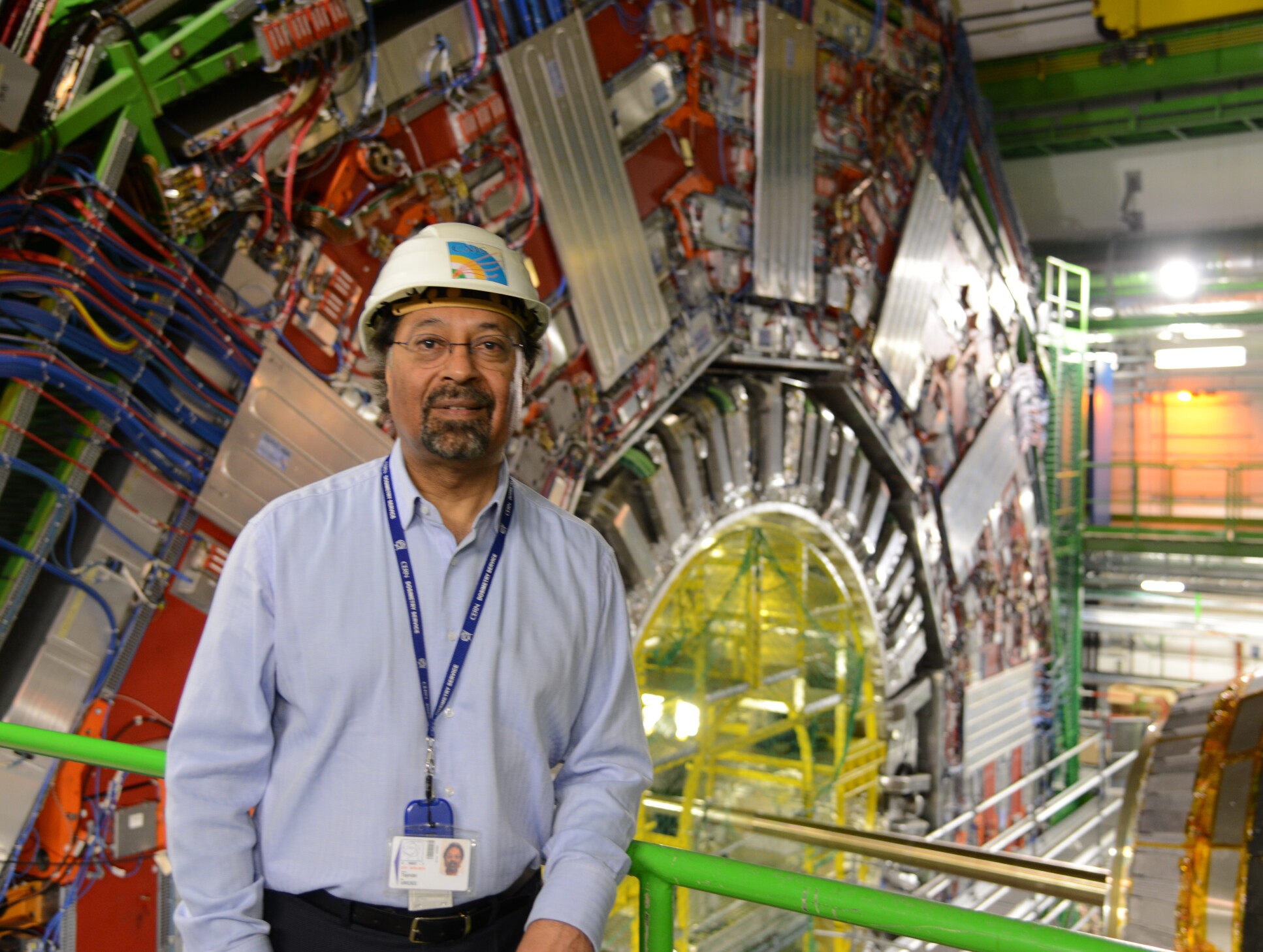 Professor Virdee in a hard hat in front of a very large machine