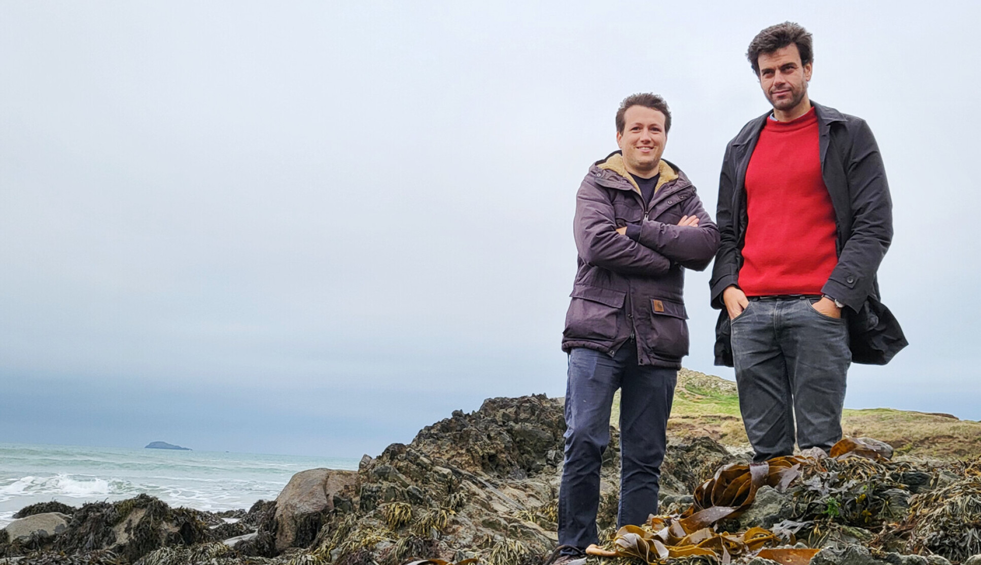Two men stand on a cliff at the seafront